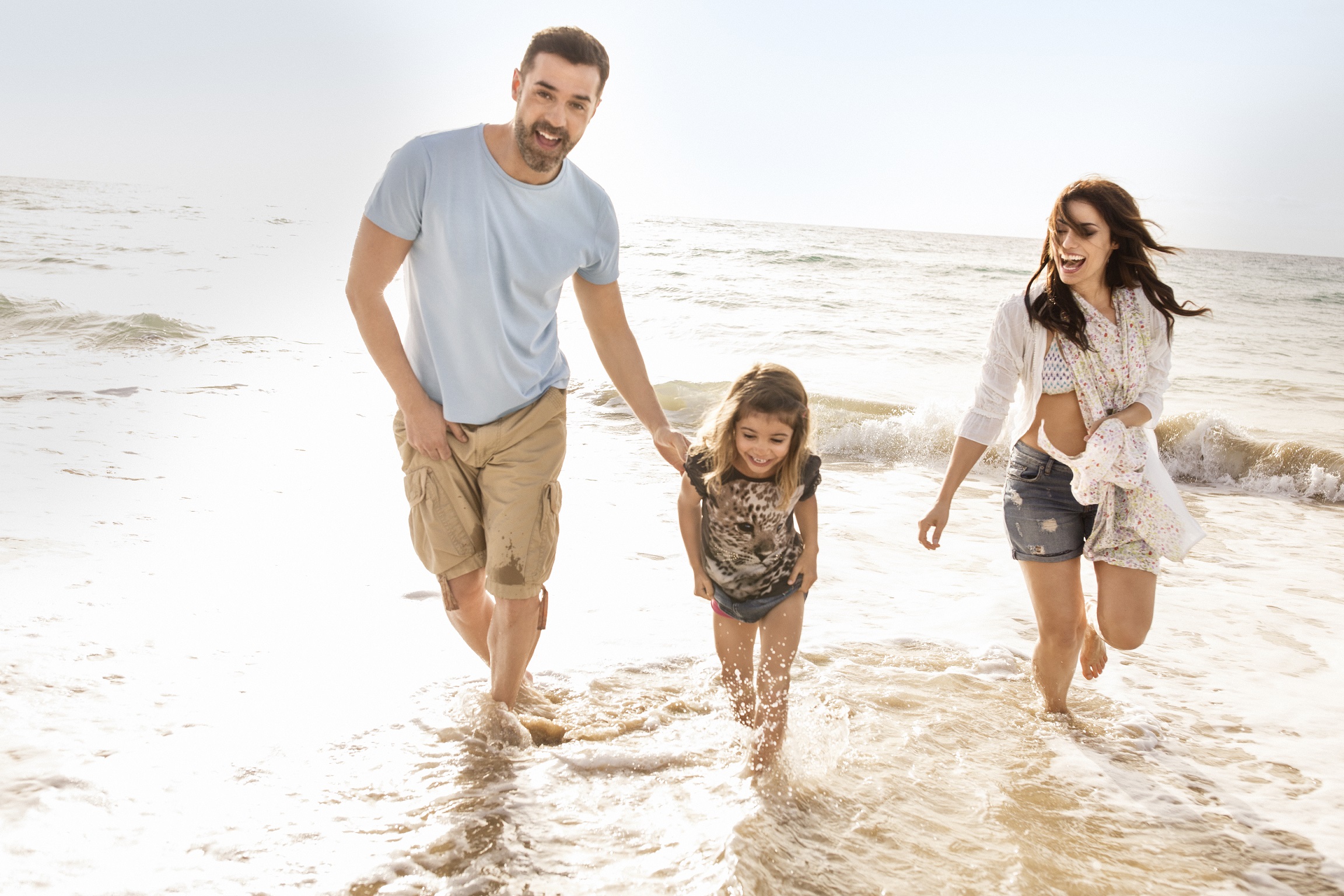 Eltern mit Kind mit den Füßen im Wasser am Strand