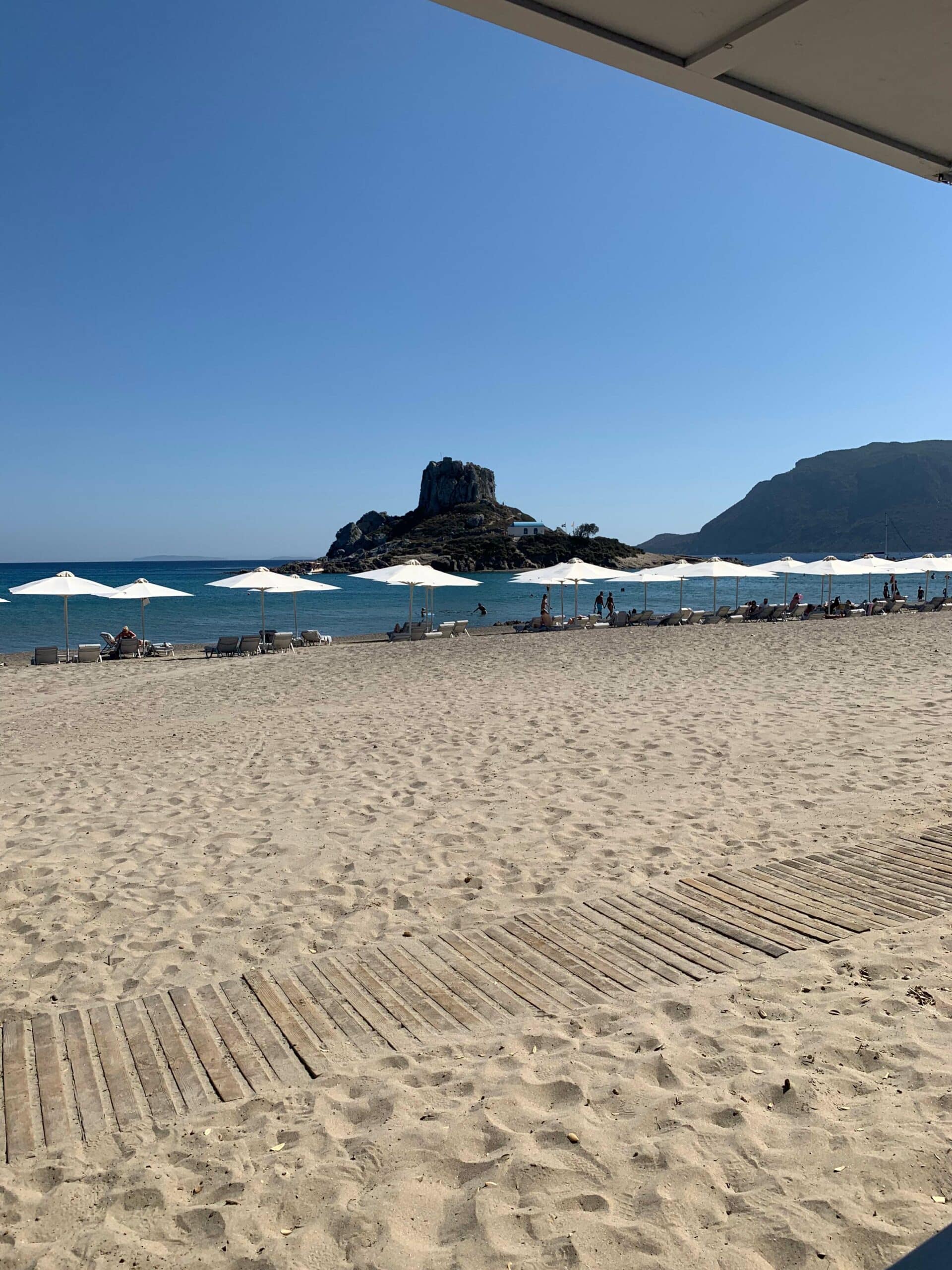 Hotelstrand mit Blick auf das Meer, Liegen mit Sonnenschirmen und Felsen im Hintergrund