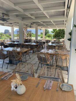 Überdachte Sitzmöglichkeiten des Restaurants mit gedeckten Tischen und Blick auf den Hotelgarten und das Meer